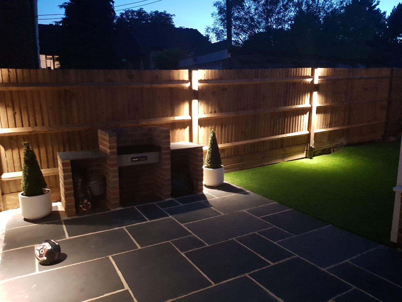 Lit close-board fencing above a slate patio at dusk
