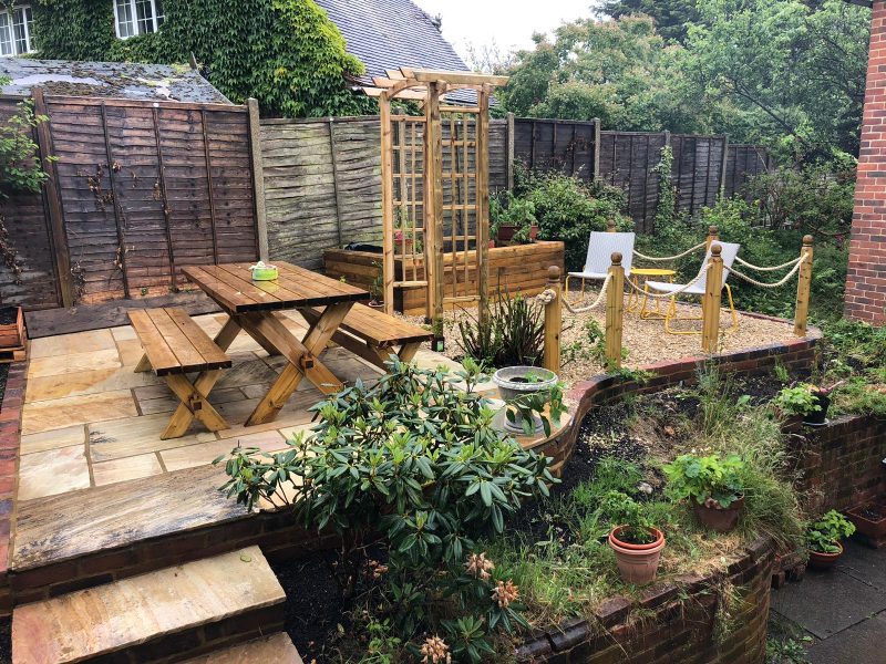 Sandstone patio with brick raised beds, timber arbour and a gravel seating area