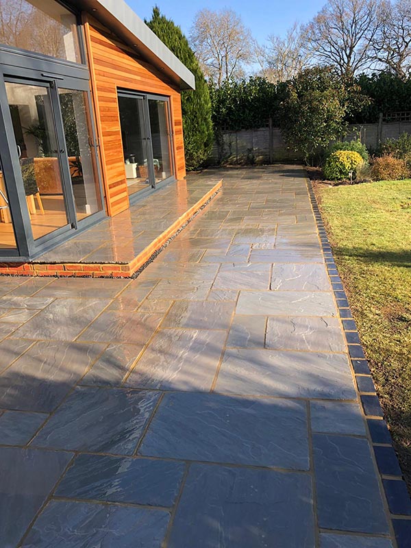 Grey sandstone patio beside a timber-clad garden room in Guildford