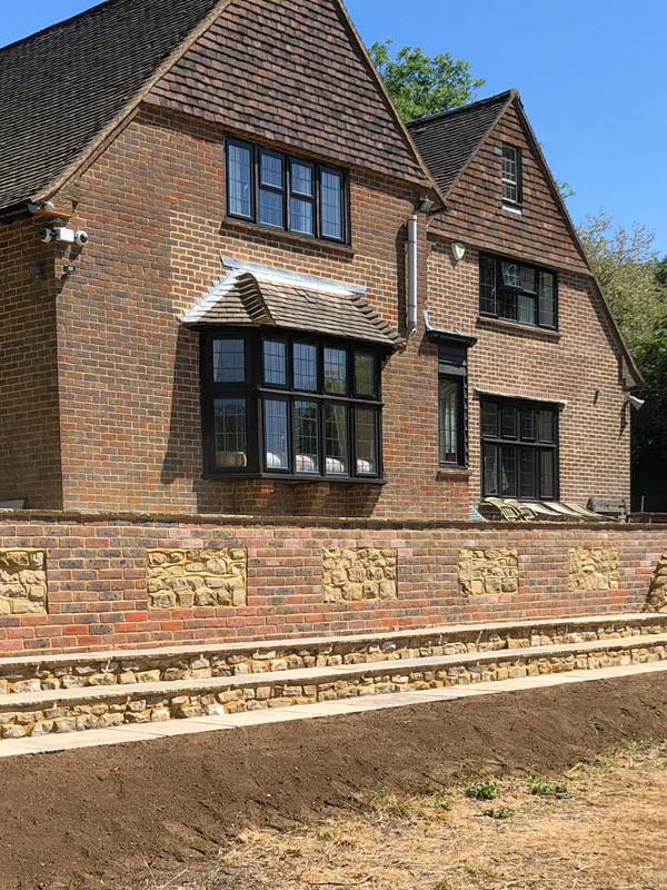 Brick and Bargate stone retaining wall in front of a tile-hung house